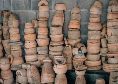 An array of handmade clay pottery pieces stacked against a cement wall, showcasing rustic craft.