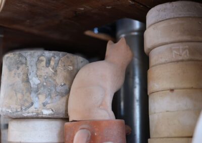 A clay cat sculpture placed among various stacked stone pots in a rustic setting.