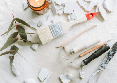 A flat lay of artisan tools, a paintbrush, eucalyptus leaves on a textured surface.