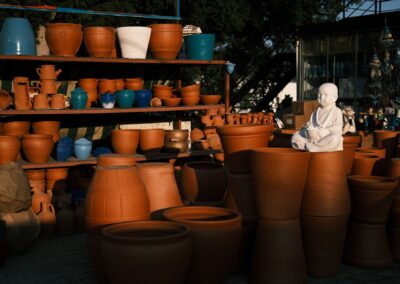 A collection of clay pots and sculptures in warm lighting on wooden shelves, showcasing handmade art.